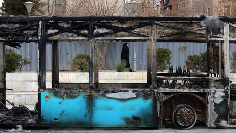Una mujer iran� vestida con el chador negro pasa ante un bus calcinado en unas protestas que cesaron hace d�as