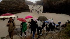 Turistas con paraguas en la playa de las Catedrales
