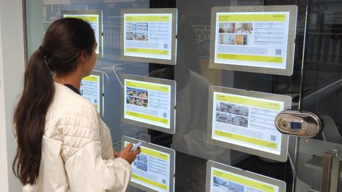 Una joven consulta los anuncios del escaparate de una inmobiliaria en una imagen de archivo