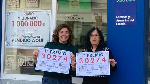 Laura (izquierda) y María José, empleadas de Loterías Galicia, en Ares, con el cartel del premio de hoy y, en la cristalera, el del 14 de diciembre