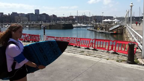 Una valla cierra el acceso a una de las rampas del Puerto Deportivo mientras al fondo se celebra el acto de izado de la Bandera Azul
