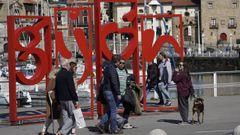 Turistas ante el rótulo con el nombre de la ciudad en el Puerto Deportivo de Gijón