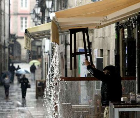 Un hostelero retira el agua de lluvia de su toldo en Lugo, donde ya ha llovido 20 días en marzo.