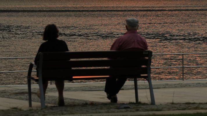 Una pareja de personas mayores sentadas frente al mar