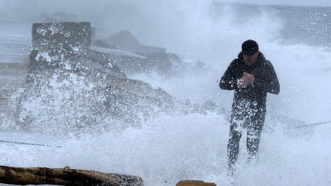 Un camina entre las olas este domingo en la playa de San Juan de Nieva en una jornada marcada por fuertes rachas de viento