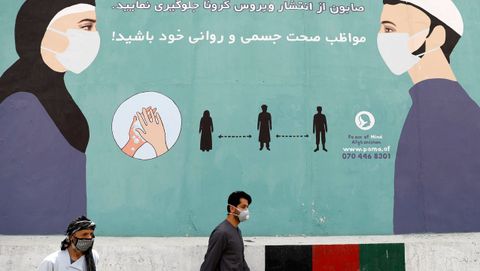 Un hombre afgano con una mscara facial protectora pasa junto a una pared pintada que advierte sobre el covid-19