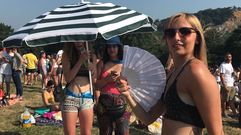 Una joven se abanica contra el calor mientras dos amigas se ocultan del sol con una sombrilla en Pola de Siero. Carm�n
