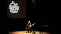 Amancio Prada dando un concierto con su guitarra y la imagen de Rosal�a de Castro de fondo