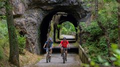 Dos personas en bicicleta pasan por uno de los t�neles sobre una antigua v�a de ferrocarril minero, situado en pleno trazado de la V�a Verde de la Senda del Oso