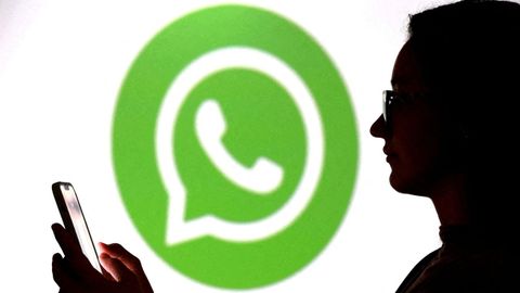 Unha persona mirando o m�bil co logo de WhatsApp ao fondo