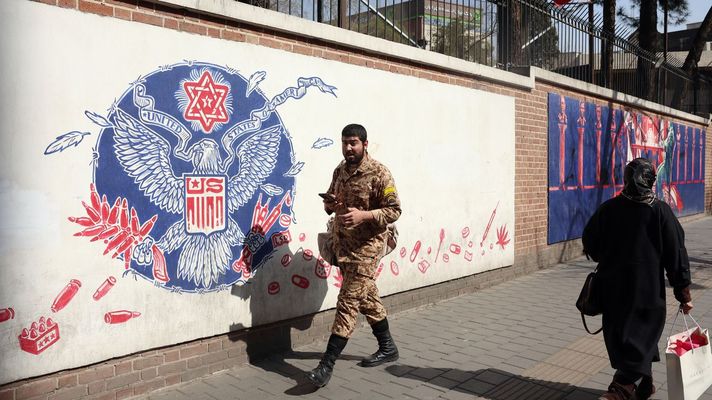 Un soldado y una mujer caminan frente a un mural antiamericano en una calle de Teher&aacute;n.
