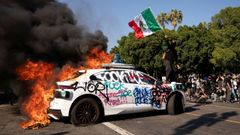 Un manifestante enarbola una bandera de Mxico subido a un coche incendiado, durante las protestas en Los ngeles