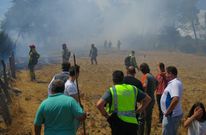 Un guardia Civil y varios vecinos, en un prado junto al incendio en el que trabajan los brigadistas. 