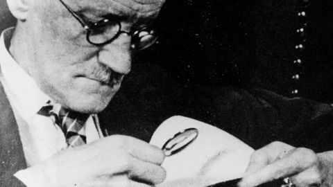 El escritor James Joyce examinando con lupa un documento.