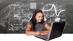 Una ni�a observa un ordenador frente a una pizarra con s�mbolos matem�ticos