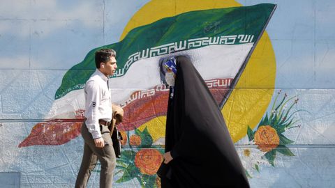 Una mujer camina frente a un mural iran en Tehern.